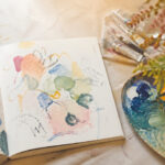 抽象的な色と線が自由に描かれたスケッチブックと、色鮮やかな絵の具のパレット
